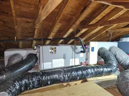 Insulated HVAC ducts and furnace in an attic with exposed wooden rafters