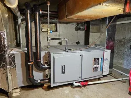 Mechanical equipment and ductwork in a basement utility room, with a white furnace and exposed pipes.
