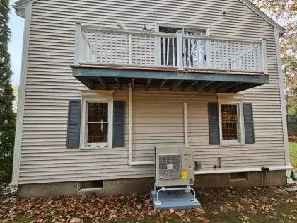 Back of a beige two-story house with a small second-floor balcony and a window air conditioner unit.