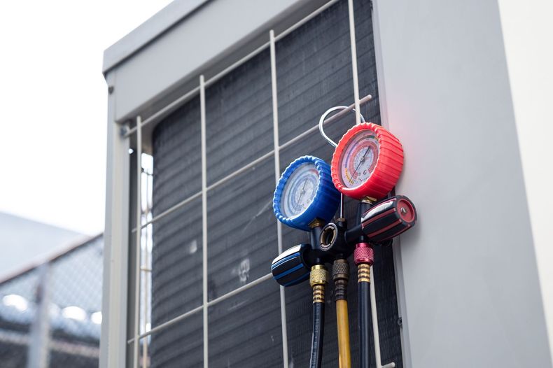 Color-coded HVAC gauges hanging on an outdoor air-conditioning unit