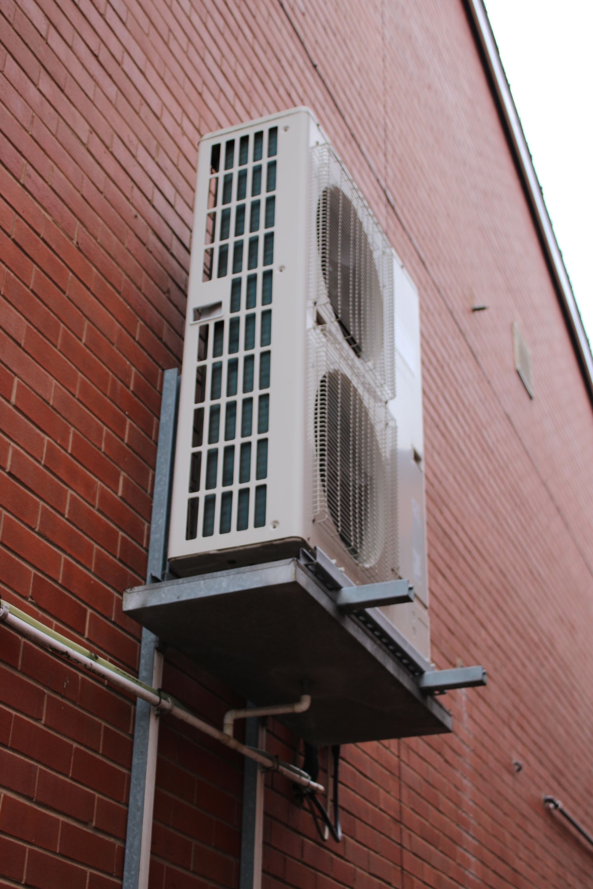 Wall-mounted dual air conditioner units on a red brick building exterior.