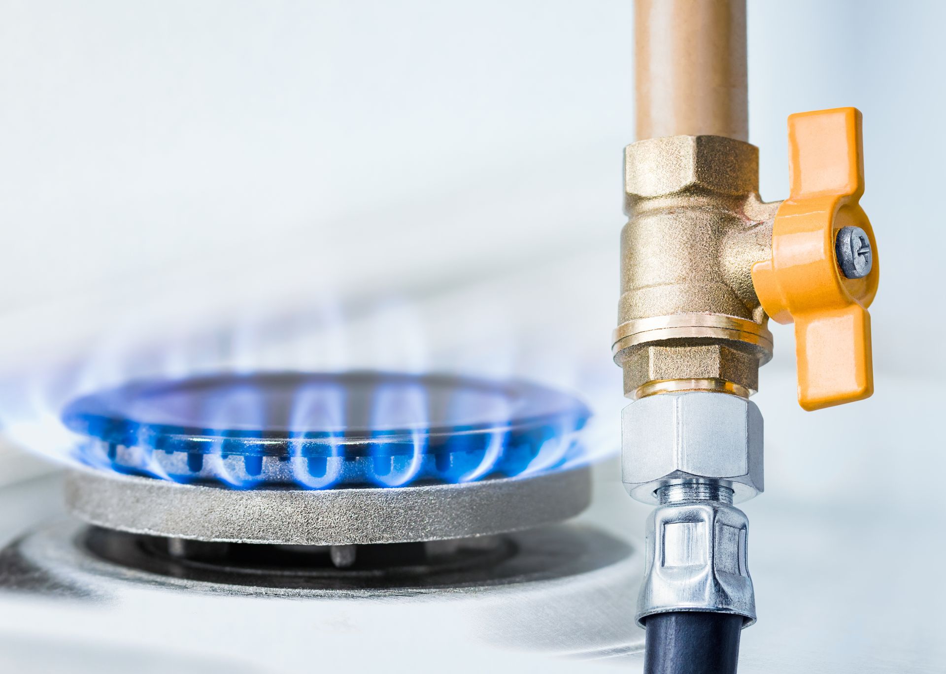 Blue gas flame on a stovetop burner with a yellow shutoff valve and copper pipe