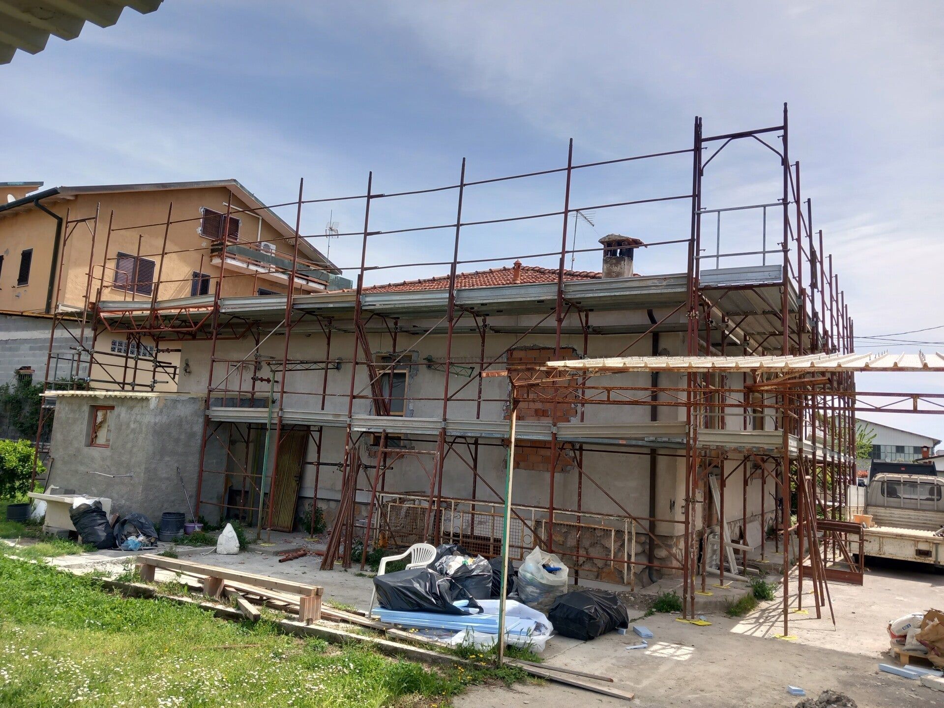 Casa in costruzione con impalcature e materiali edili all'esterno di un edificio beige a due piani.