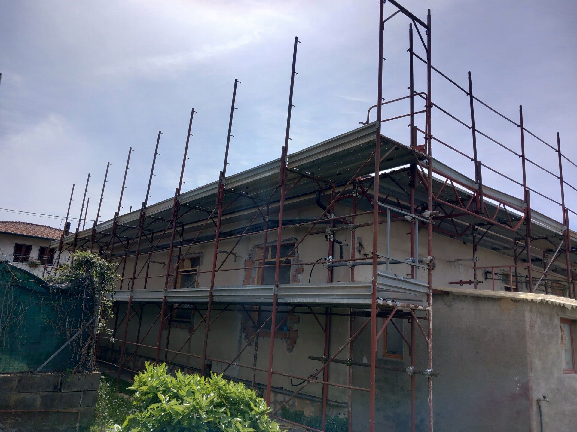 Impalcature attorno a un edificio in costruzione, con la struttura del tetto e le pareti in cemento a vista.