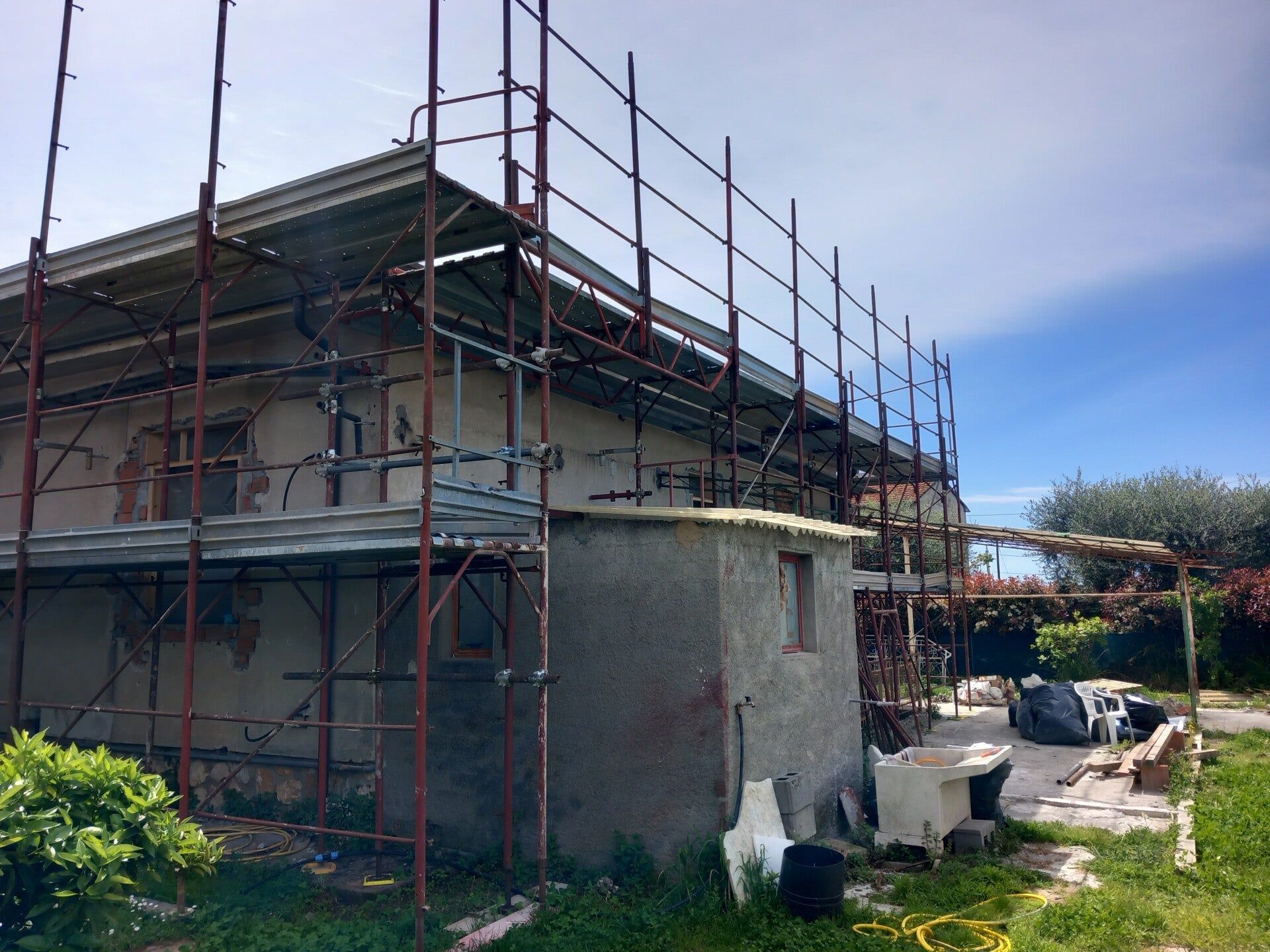 Casa in costruzione con impalcature blu e esterni parzialmente rifiniti sotto un cielo limpido