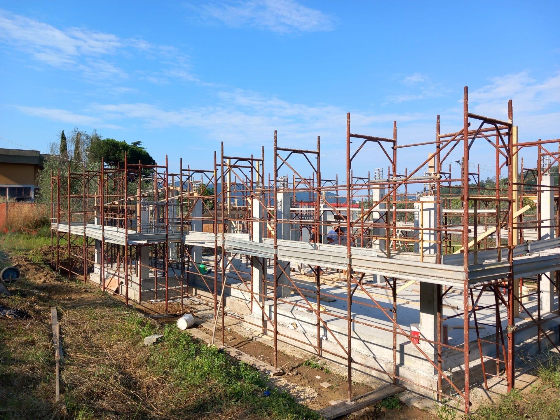 Casa parzialmente costruita con impalcature e operai sotto un cielo azzurro.