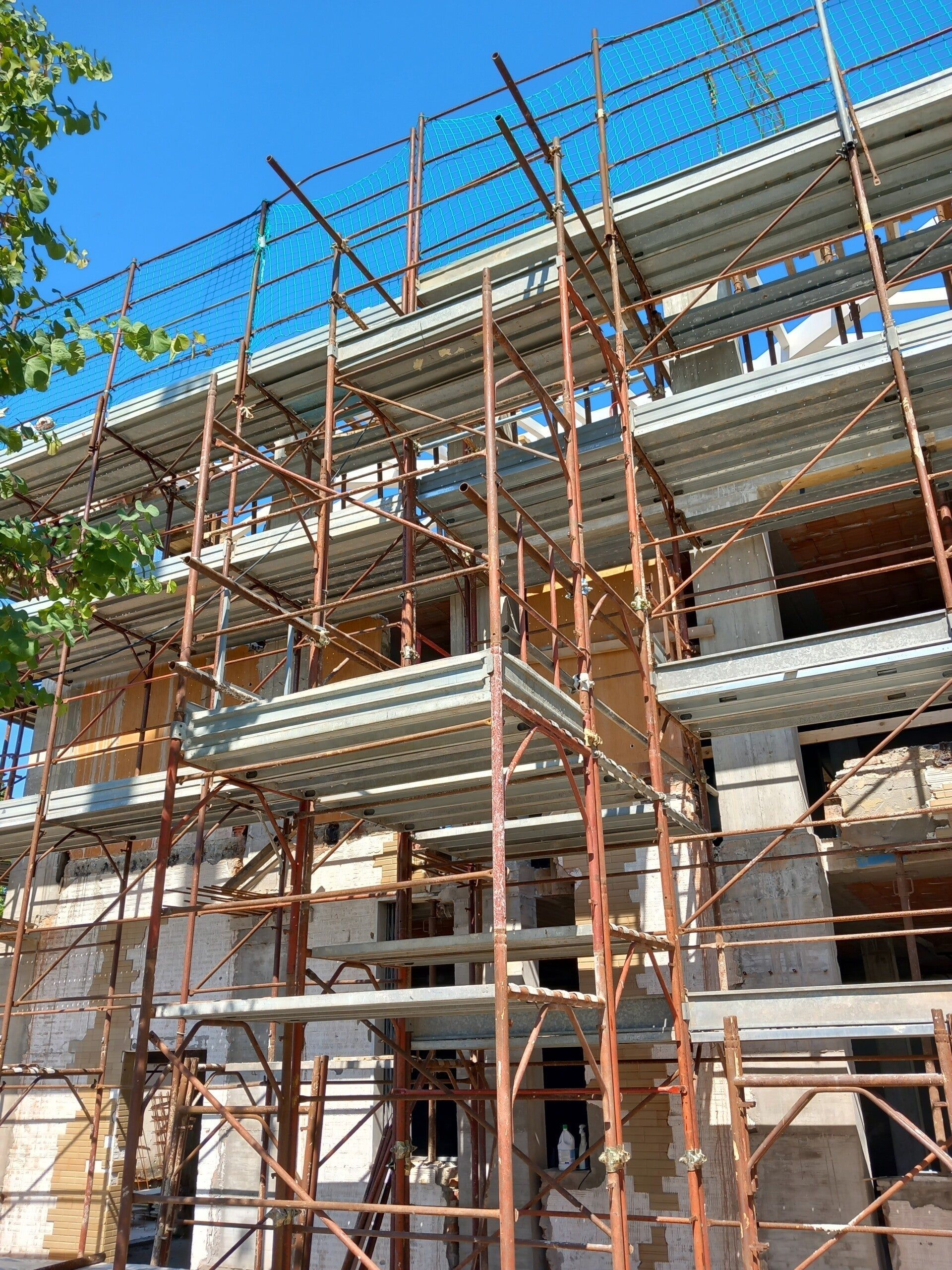 Impalcature attorno a un edificio a più piani in costruzione, sullo sfondo di un cielo azzurro.