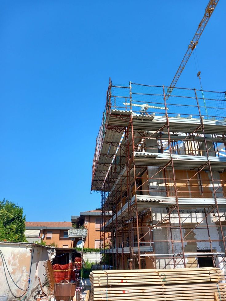 Ponteggi in costruzione con legname accatastato e una gru sullo sfondo di un cielo azzurro limpido.