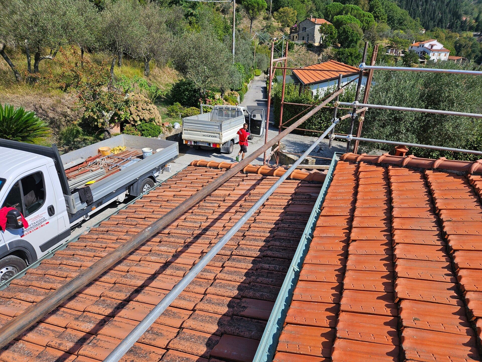 Operai su un tetto di tegole di terracotta vicino a un camion su una ripida strada in collina