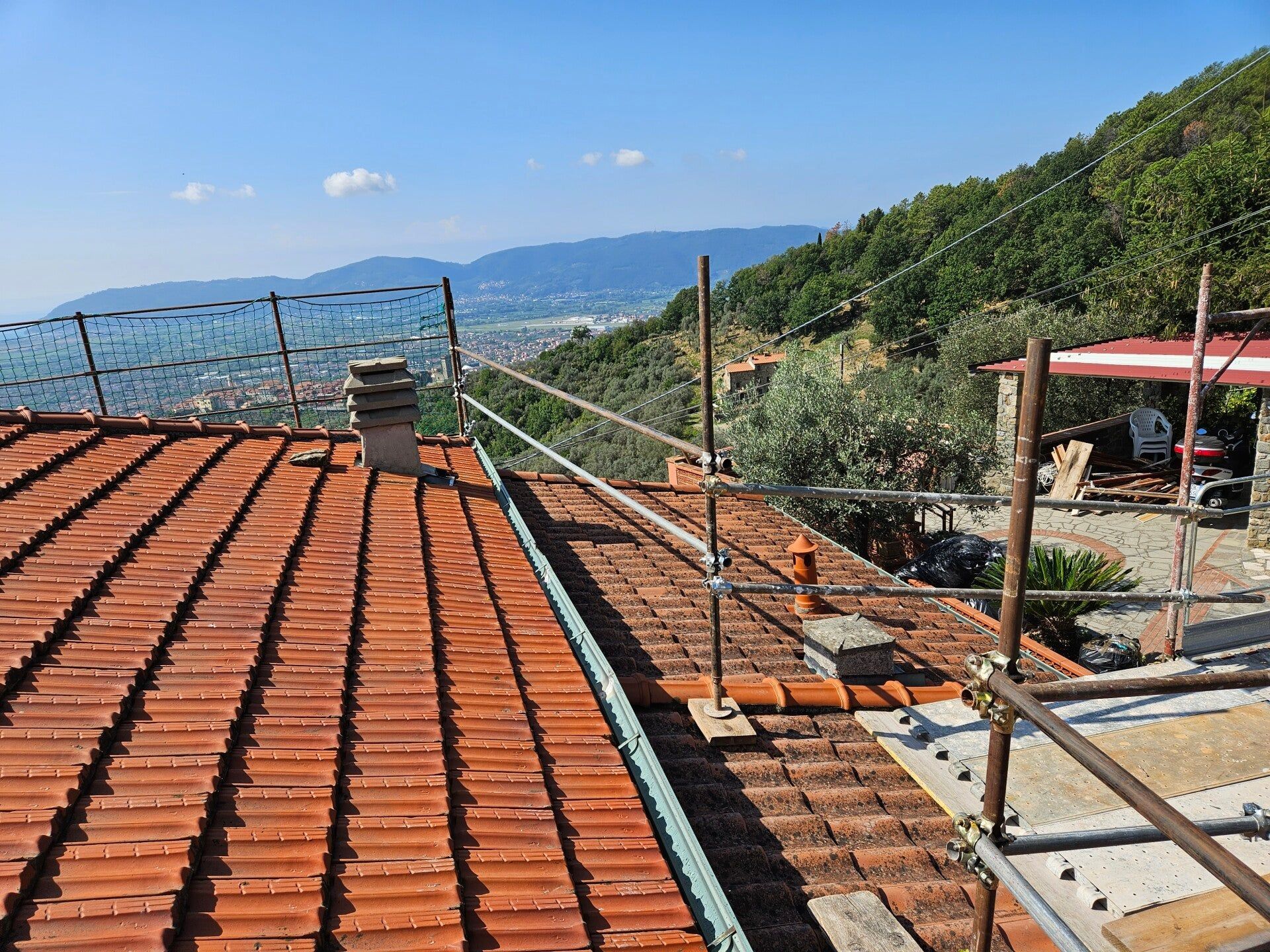 Tettoia con tegole in terracotta affacciata su una collina costiera e sul mare blu, con impalcature sulla destra.
