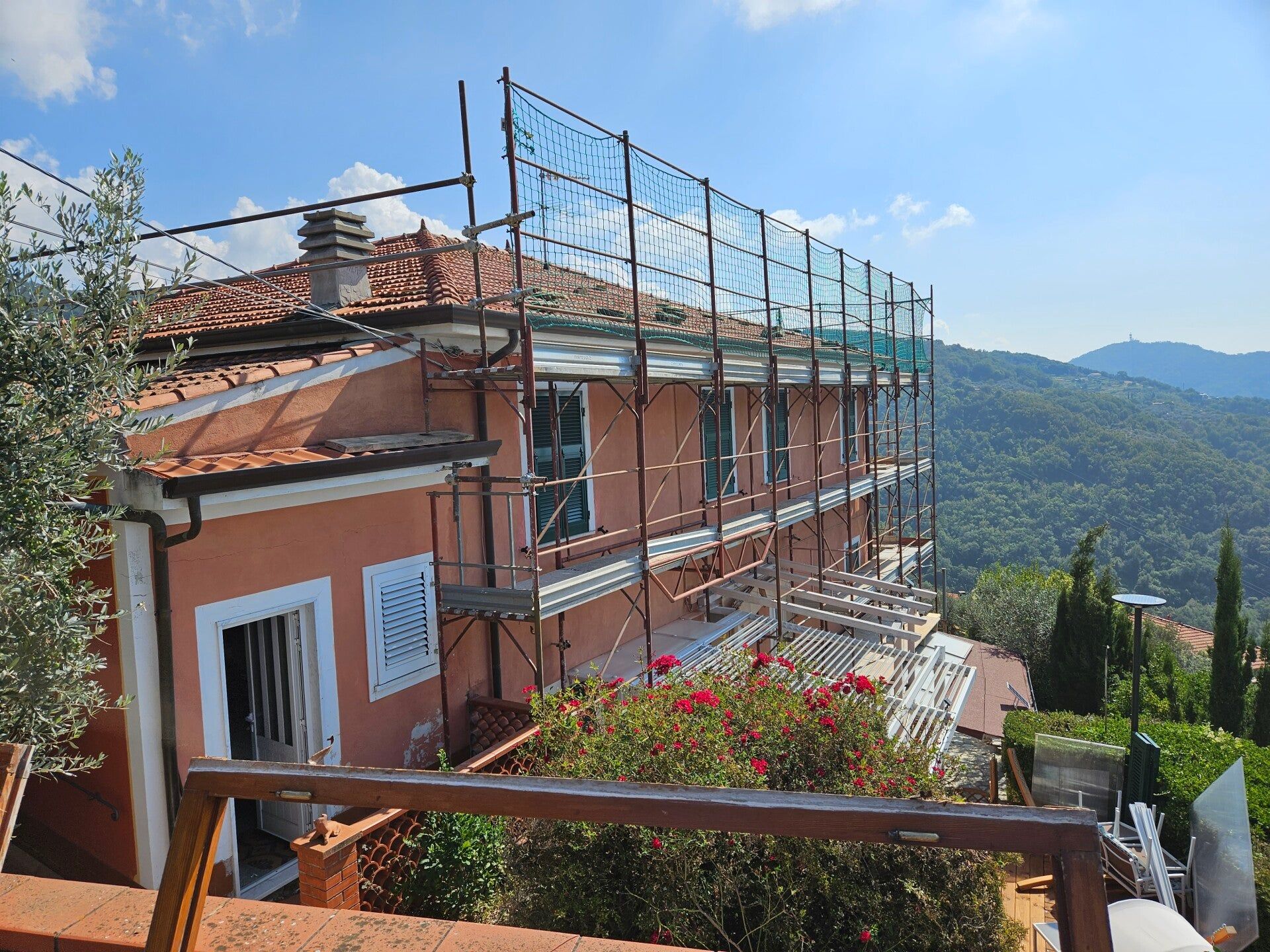 Casa in mattoni impalcata, costruita su un pendio con montagne e cielo azzurro sullo sfondo.