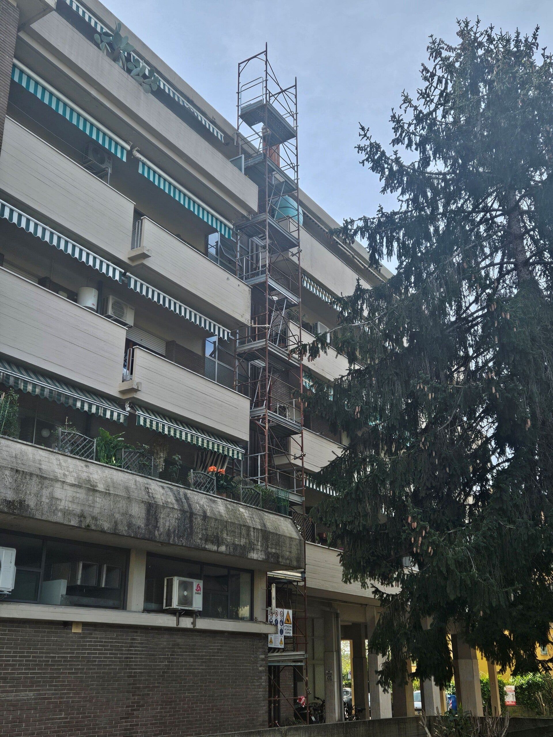 Edificio a più piani con balconi e torre di telecomunicazioni accanto a un albero alto al crepuscolo