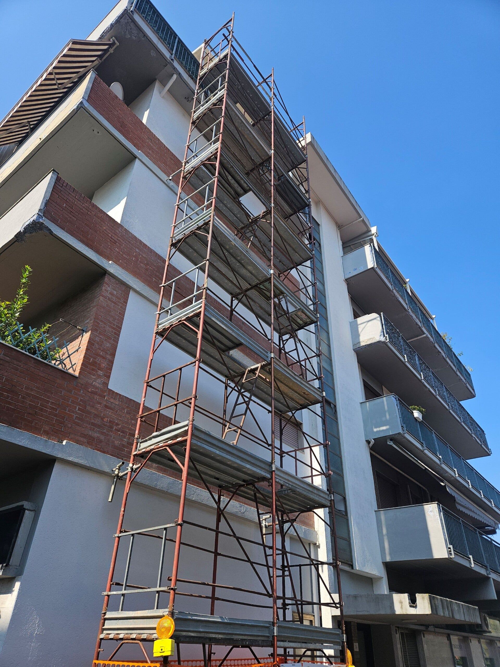 Impalcature su un edificio residenziale in mattoni in costruzione, sullo sfondo di un cielo azzurro.