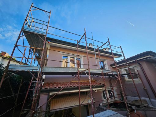 Impalcature attorno a una casa a due piani in costruzione sotto un cielo azzurro e limpido.