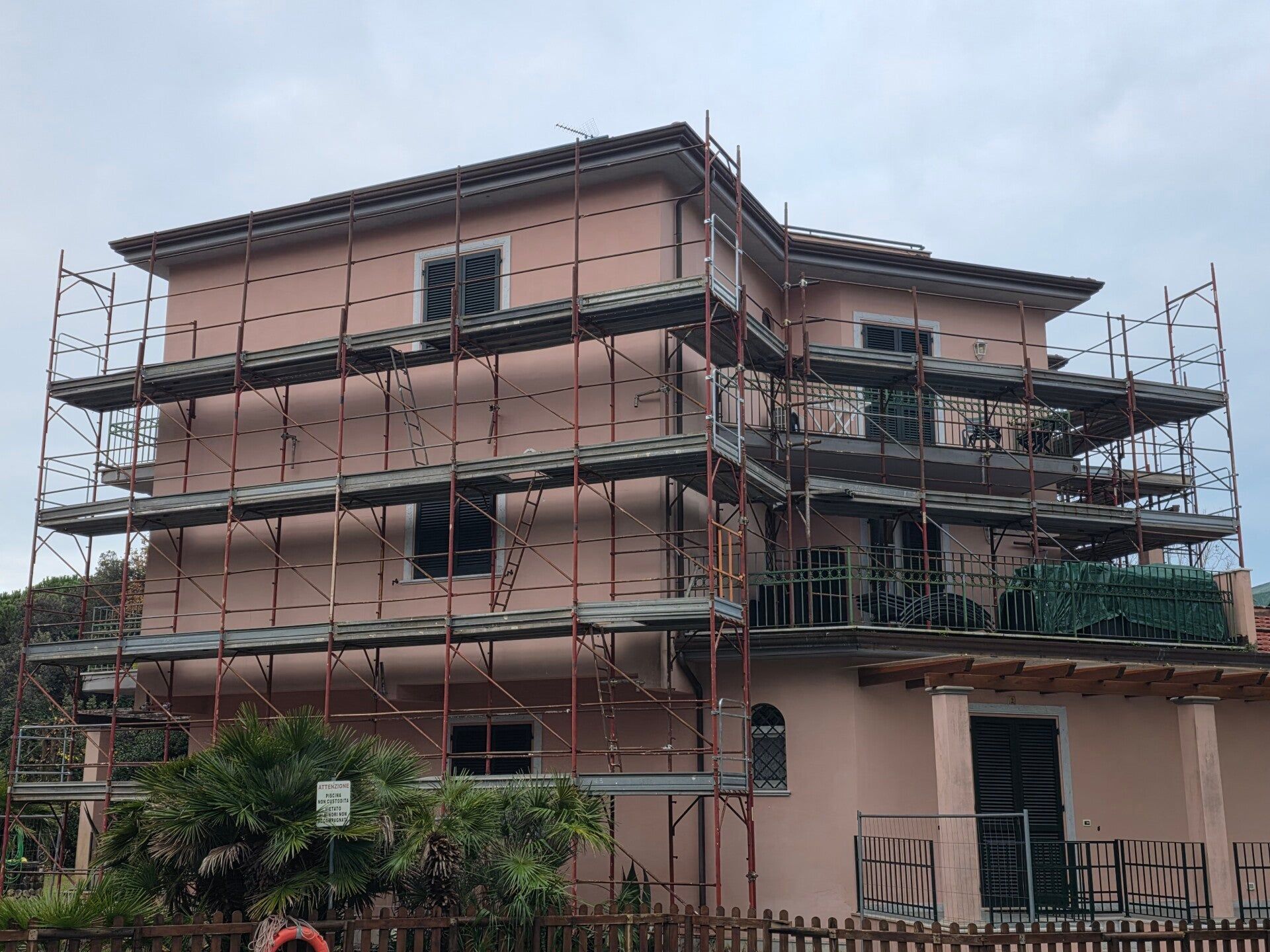 Edificio di tre piani in costruzione con impalcature intorno alla facciata e finestre aperte.