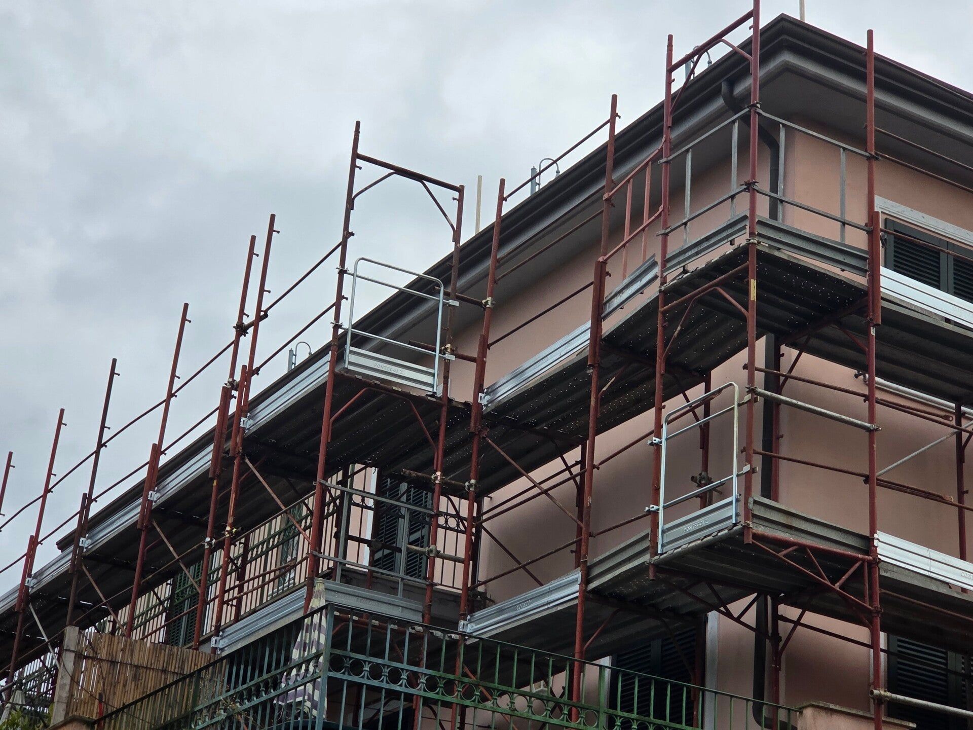 Edificio a più piani in costruzione con impalcature rosse contro un cielo nuvoloso.