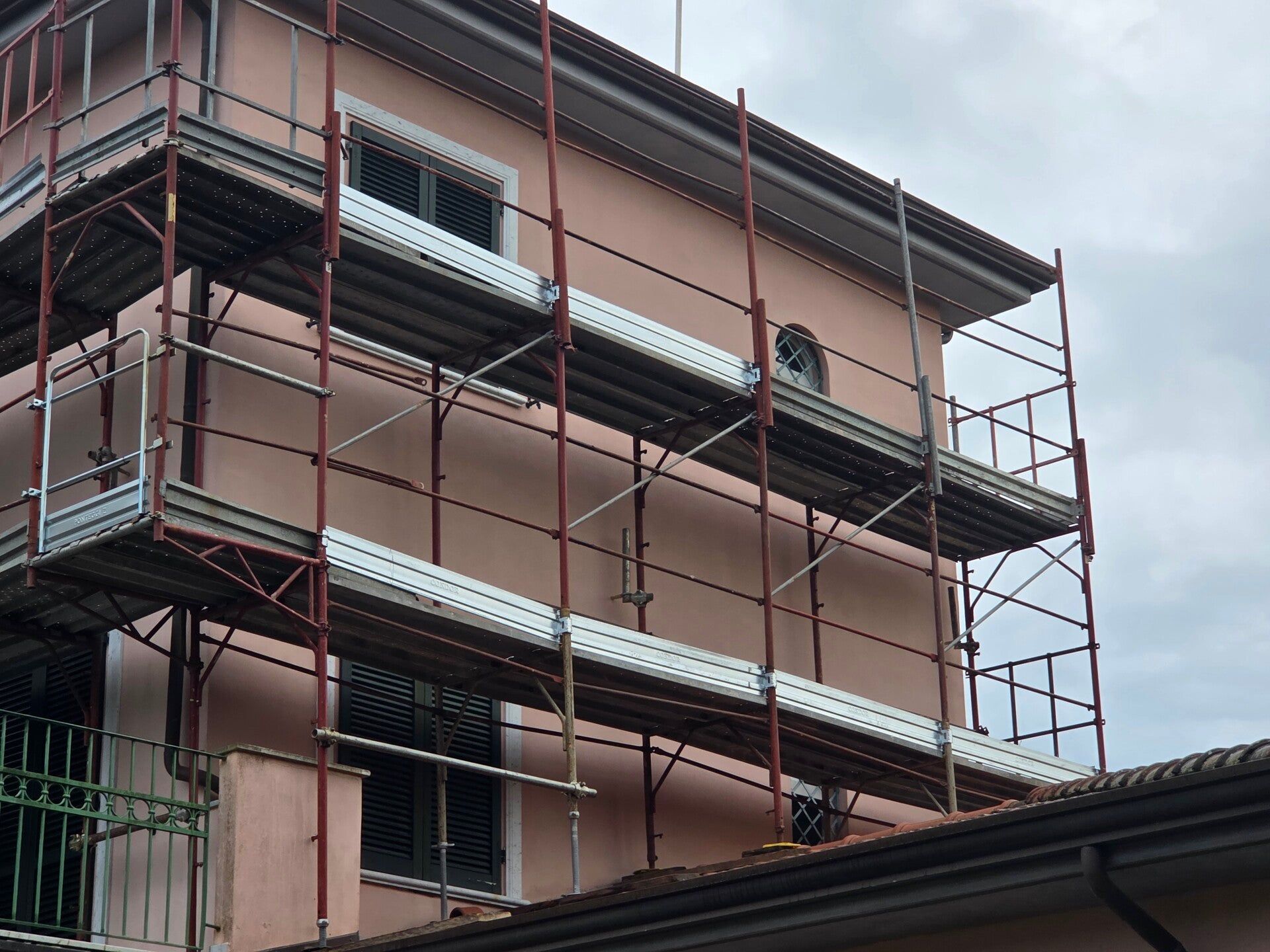 Edificio di tre piani con pareti rosa e impalcature metalliche durante i lavori di ristrutturazione esterna.