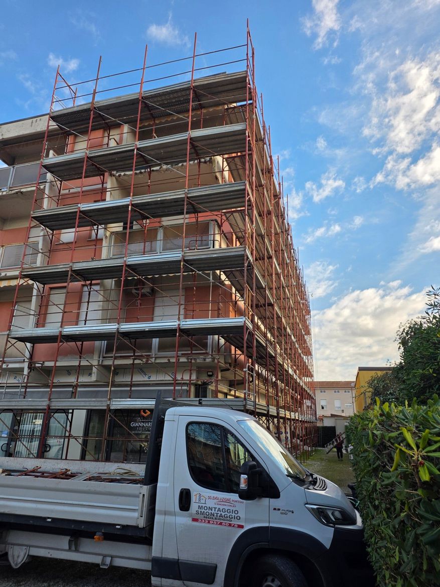 Un'impalcatura circonda un edificio in mattoni rossi in costruzione, con un camion bianco parcheggiato davanti.