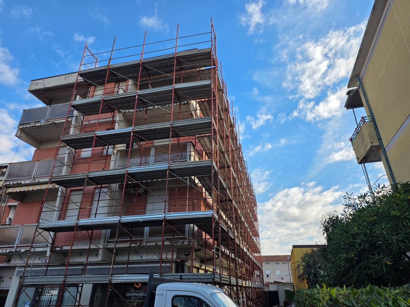 Un palazzo residenziale in costruzione, con impalcature, si staglia contro un cielo azzurro.