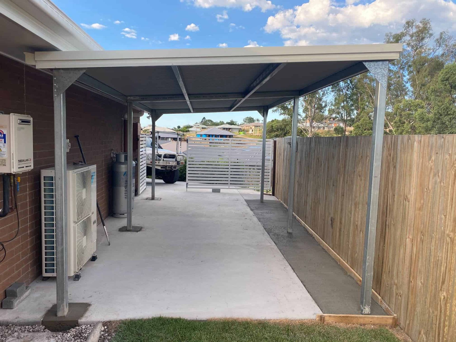 Covered carport with metal roofing and posts over a concrete driveway beside a house
