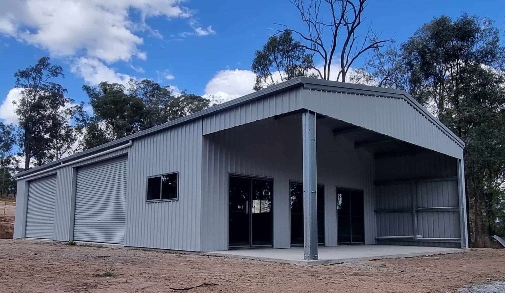A Large Metal Building With A Porch And Trees In The Background — Just Sheds In Kunda Park, QLD