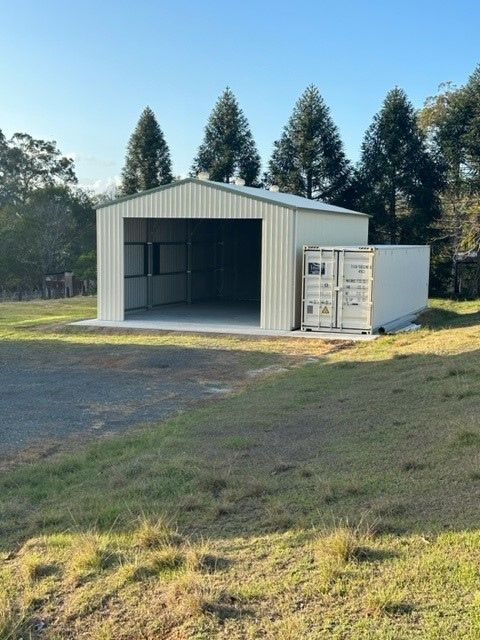 A White Building With A Shipping Container In Front Of It — Just Sheds In Kunda Park, QLD