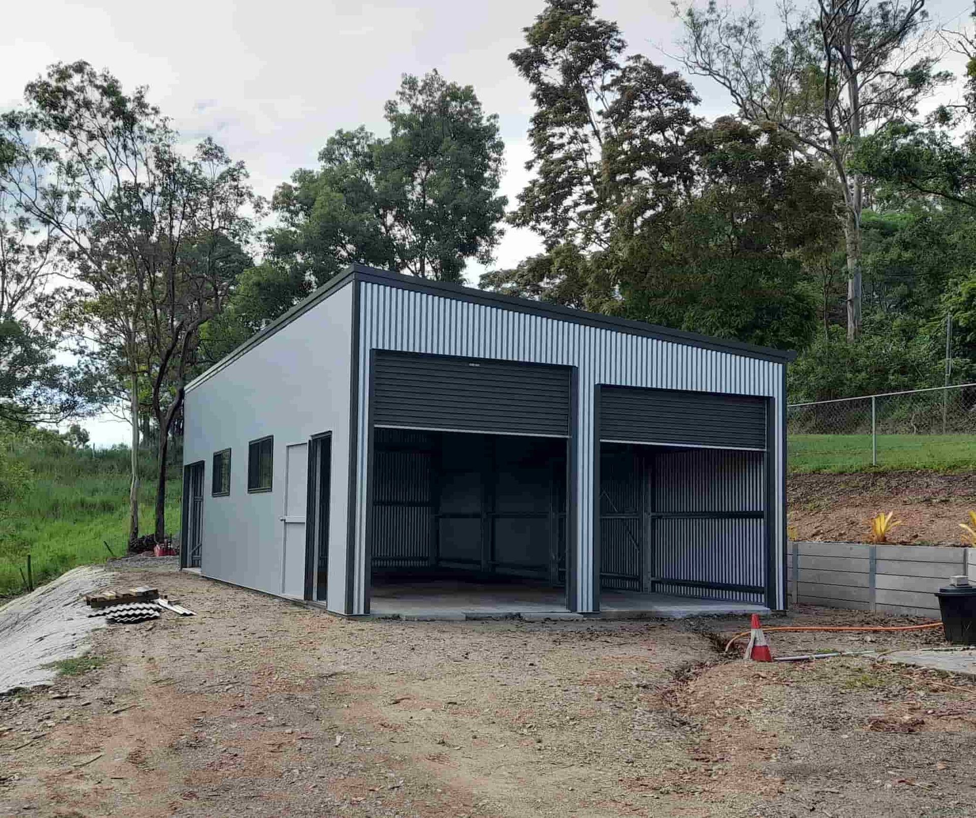 A Metal Building With Two Garage Doors Is Being Built In The Middle Of A Dirt Field — Just Sheds In Kunda Park, QLD