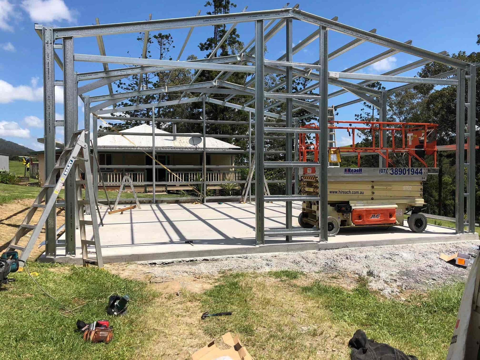 A large metal structure is being built in a grassy field. — Just Sheds In Kunda Park, QLD