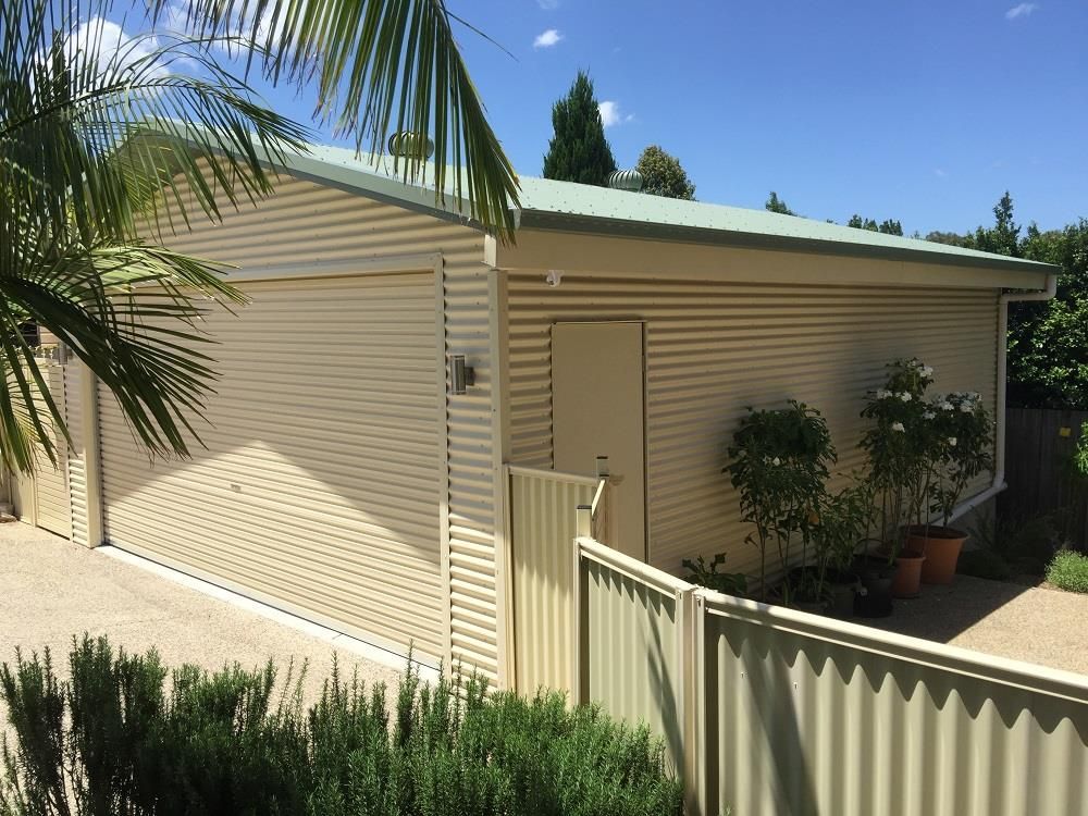A garage with a fence and a palm tree in the background — Just Sheds In Kunda Park, QLD