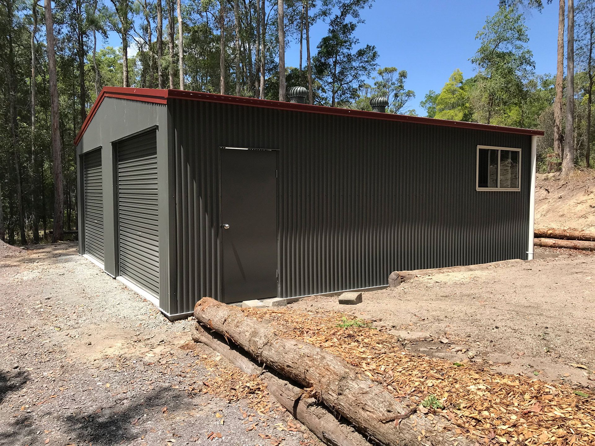 A Large Metal Building With a Red Roof is Sitting in the Middle of a Dirt Field — Just Sheds In Kunda Park, QLD
