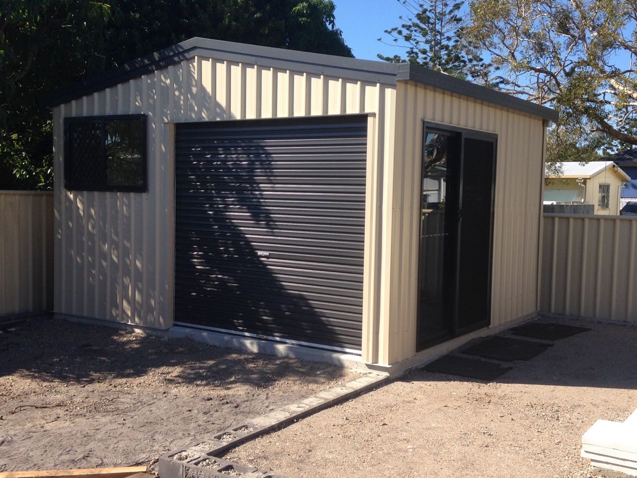 A Shed With a Black Garage Door is in a Backyard — Just Sheds In Kunda Park, QLD
