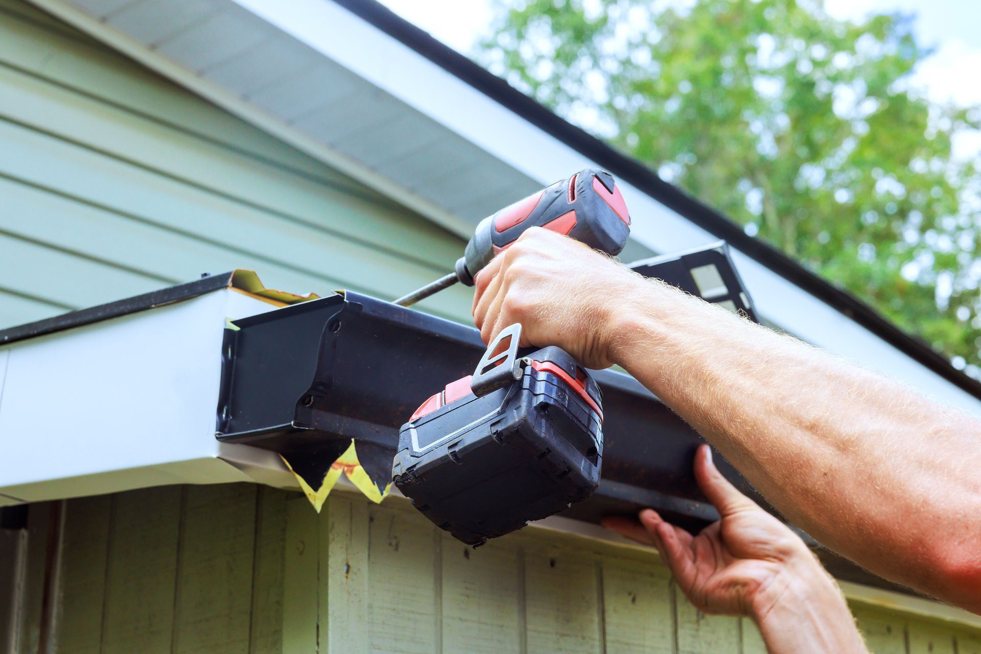 Person using a cordless drill to install a gutter on a house exterior