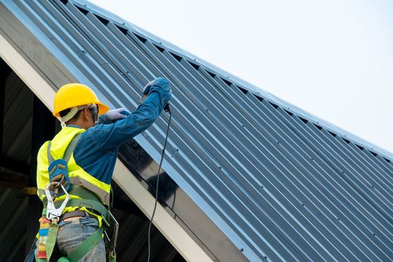 Roofer in yellow helmet and safety vest installing metal roof panels. Roofer in yellow helmet and safety vest installing metal roof panels.