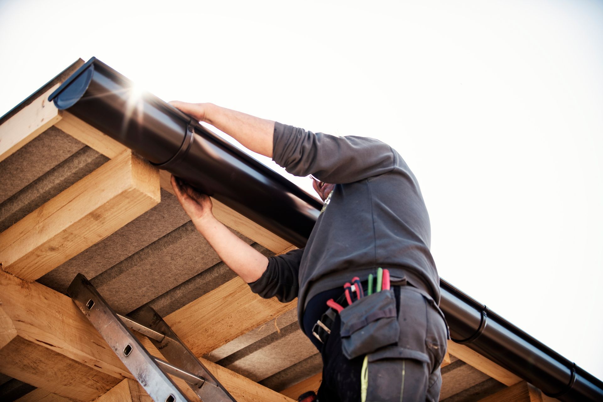The worker installs a black gutter on the wooden roof frame.
