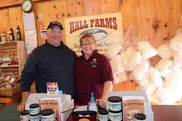 A man and woman smile behind a counter at Hall Farms, with various jars of product displayed on the checkout surface.