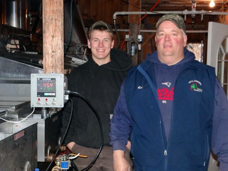 Two people in a workshop next to a temperature-controlled maple syrup evaporator with a digital reading of 45.4.