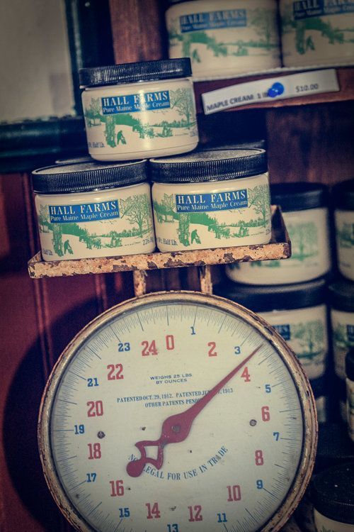 Several jars of Hill Farms maple cream sit on a vintage scale, with the needle pointing just past three.