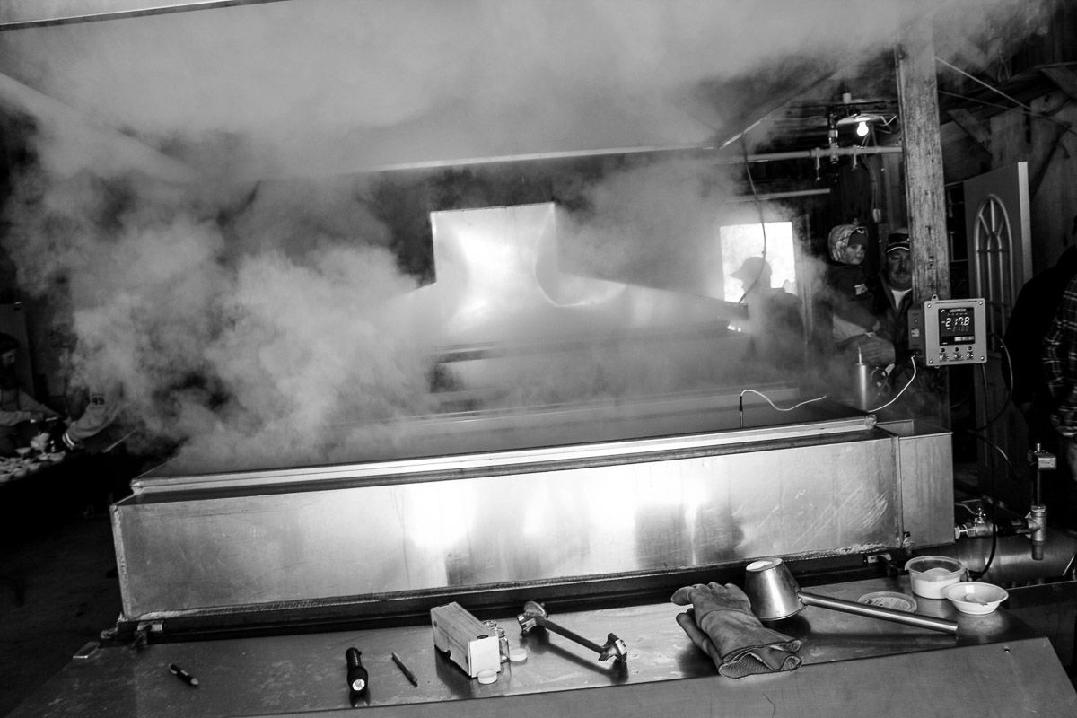 A black-and-white view of a large rectangular vat emitting thick plumes of steam inside an industrial or workspace.