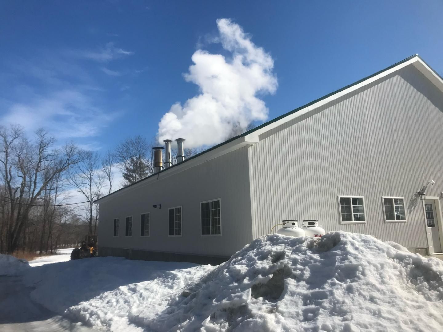 A light-gray building with steaming vents on the roof, surrounded by snow under a bright blue sky.