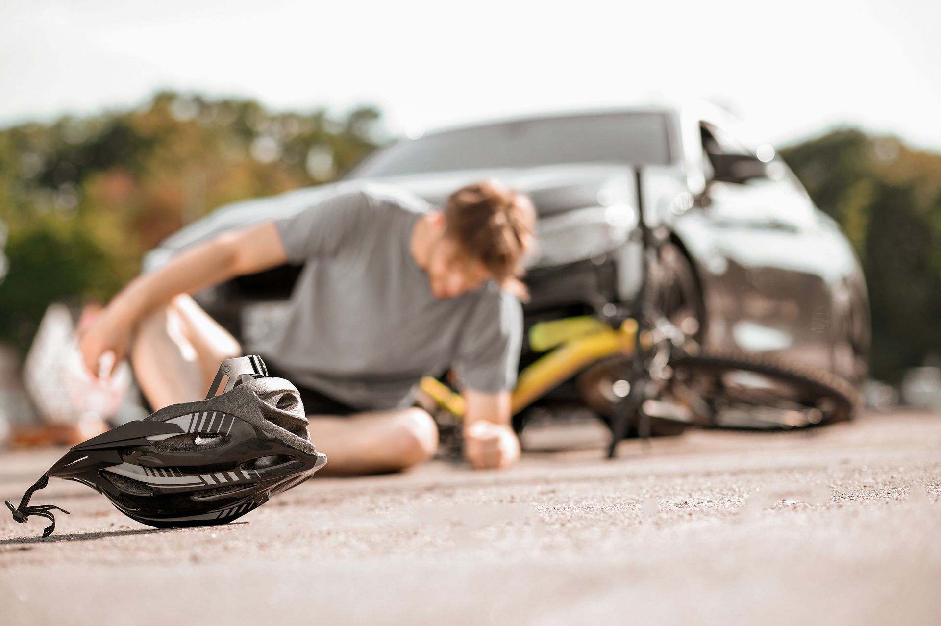 Cyclist kneeling beside a crashed bicycle on a road, with a broken wheel in the foreground