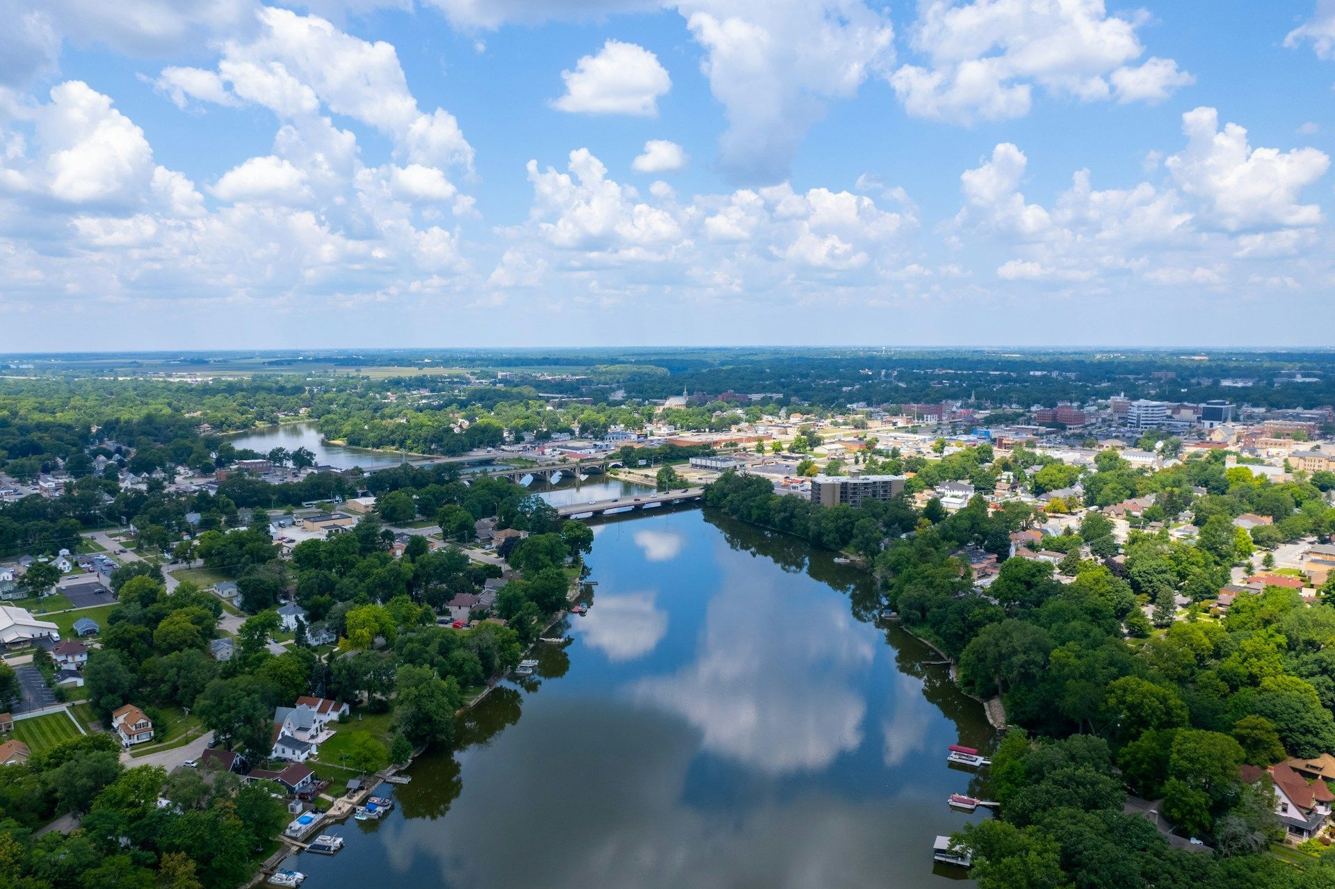 Aerial view of a calm lake surrounded by green neighborhood homes under a partly cloudy sky.