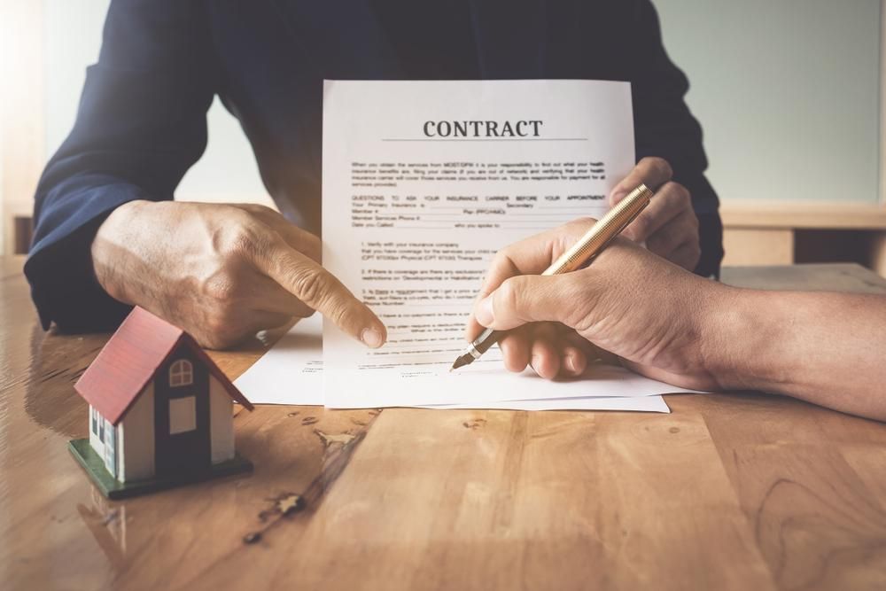 A Couple Of People Are Sitting At A Table Signing A Contract — Howells & Co Legal & Conveyancing In Cessnock, NSW