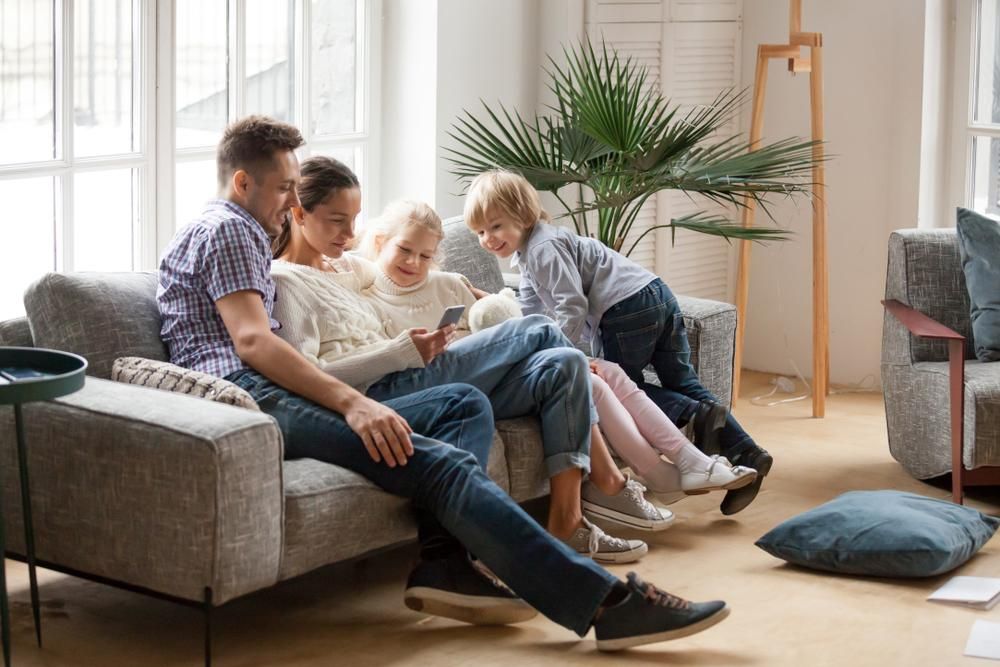 A Family Is Sitting On A Couch In A Living Room Looking At A Cell Phone — Howells & Co Legal & Conveyancing In Tamworth, NSW