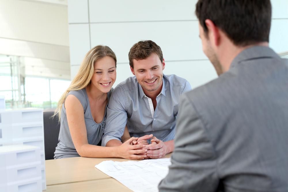 A Man And A Woman Are Sitting At A Table Talking To A Real Estate Agent — Howells & Co Legal & Conveyancing In Cessnock, NSW