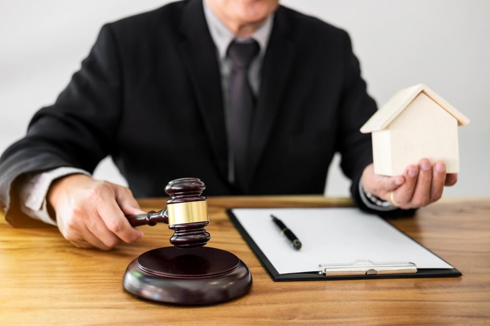 A Man In A Suit And Tie Is Holding A Gavel And A Small House — Howells & Co Legal & Conveyancing In Cessnock, NSW