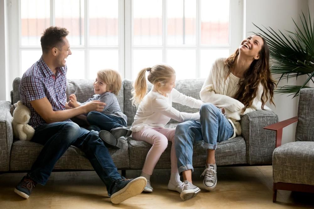 A Family Is Sitting On A Couch In A Living Room — Howells & Co Legal & Conveyancing In Cessnock, NSW