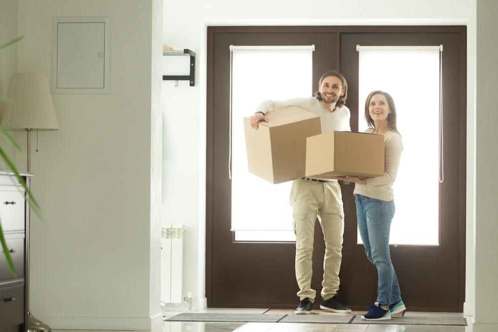 A Man And A Woman Are Carrying Cardboard Boxes Into A New Home — Howells & Co Legal & Conveyancing In Maitland, NSW
