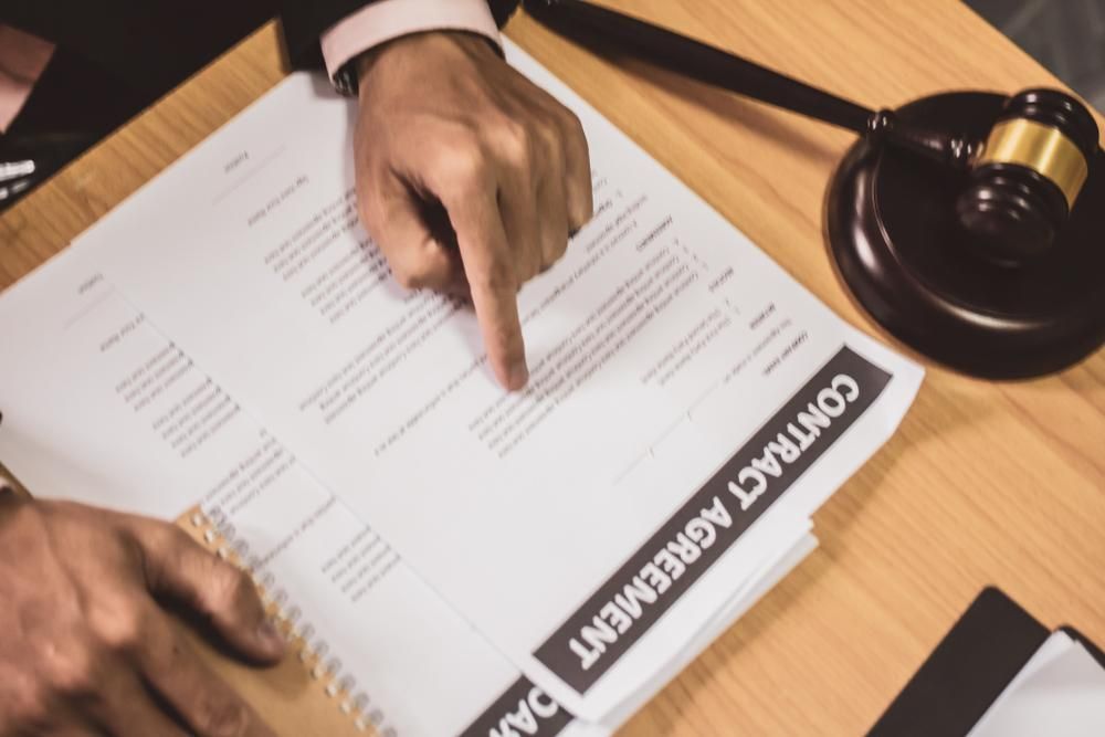 A Person Is Pointing At A Contract Agreement On A Table — Howells & Co Legal & Conveyancing In Cessnock, NSW