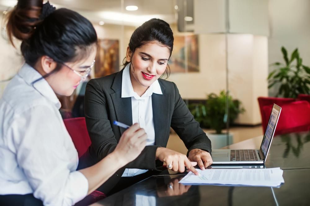 Two Women Are Sitting At A Table Looking At A Laptop — Howells & Co Legal & Conveyancing In Lake Macquarie, NSW