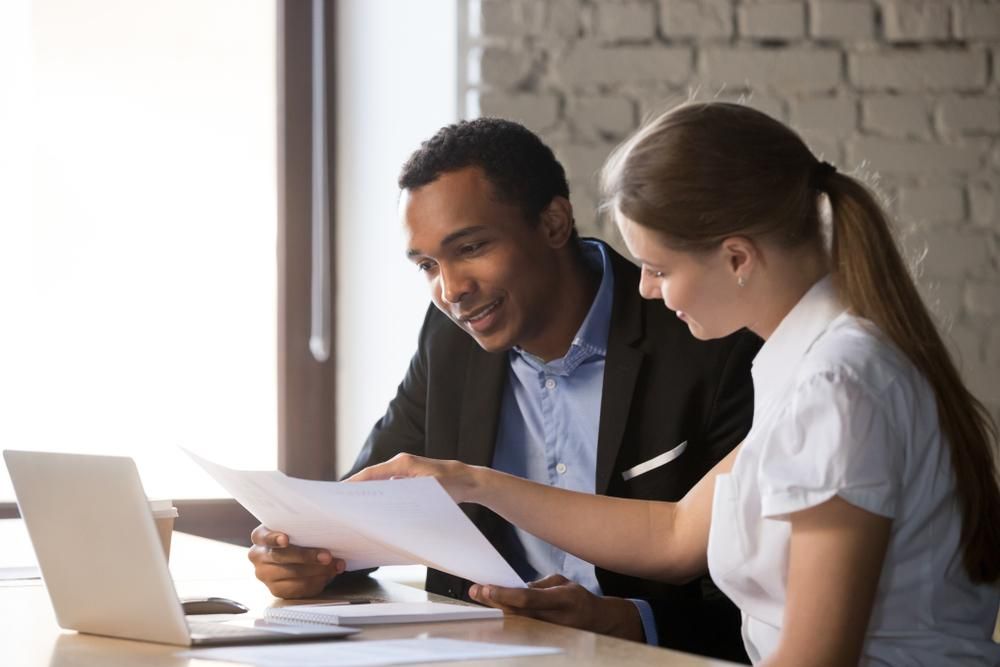 A Man And A Woman Are Sitting At A Table Looking At A Piece Of Paper — Howells & Co Legal & Conveyancing In Muswellbrook, NSW